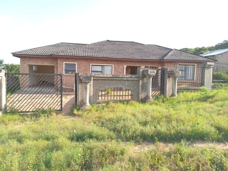 Front elevation of a single-story brick house featuring a tiled roof, integrated garage, and a partially finished perimeter wall with metal gate access.
