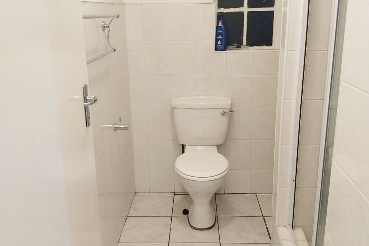 A functional bathroom featuring a toilet, shower enclosure, and neutral wall and floor tiling, offering a clean and practical space.