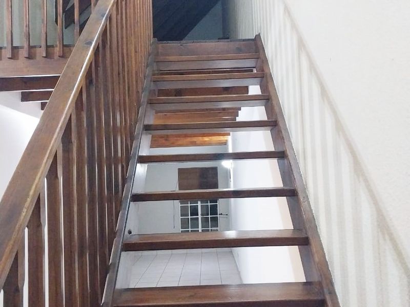 A staircase with wooden steps and balustrade leading to an upper level with exposed timber rafters and tiled flooring.