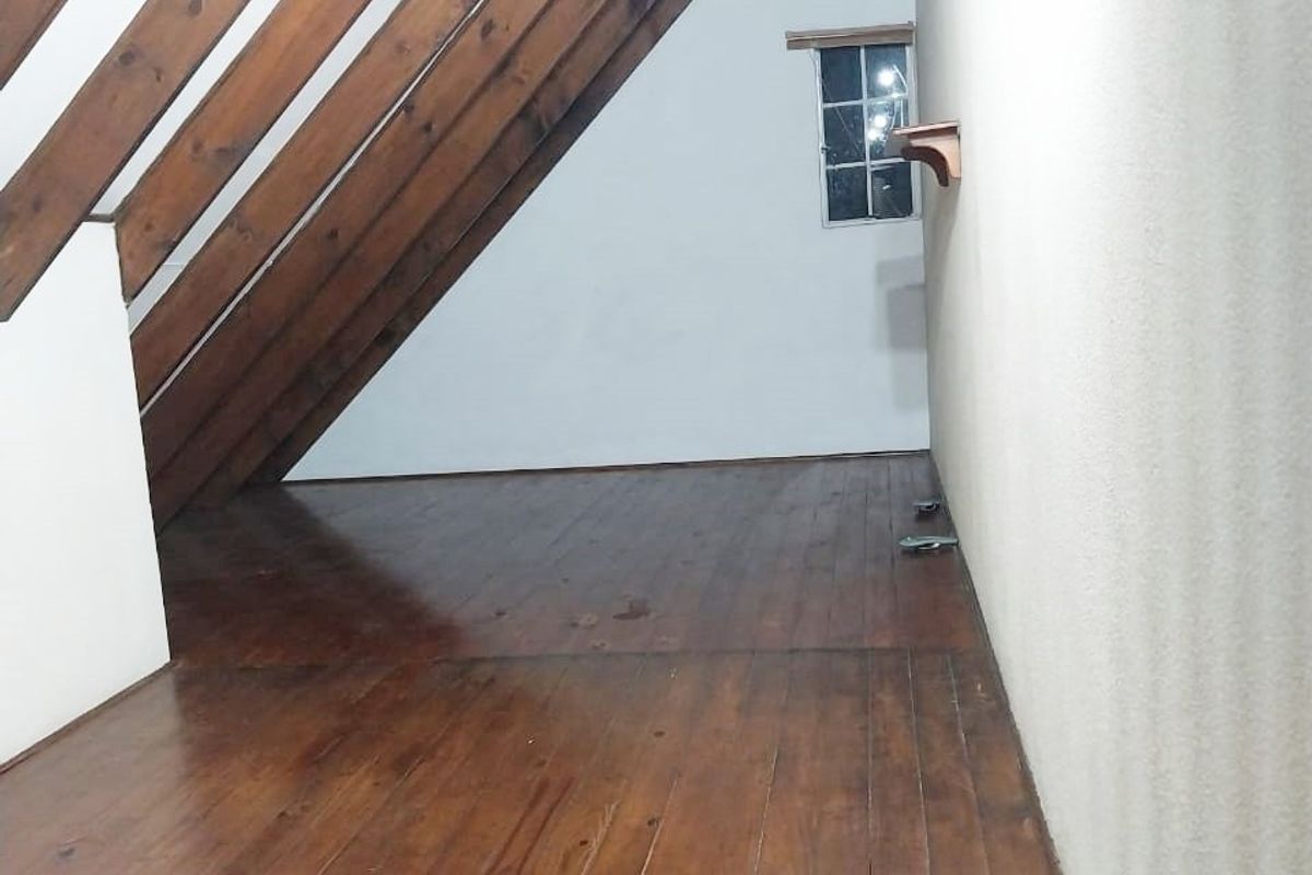 An empty attic-style bedroom featuring exposed timber rafters, polished timber flooring, and a small window, offering a cozy, character-filled space.