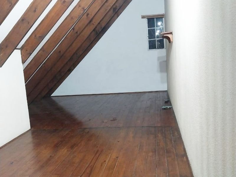 An empty attic-style bedroom featuring exposed timber rafters, polished timber flooring, and a small window, offering a cozy, character-filled space.