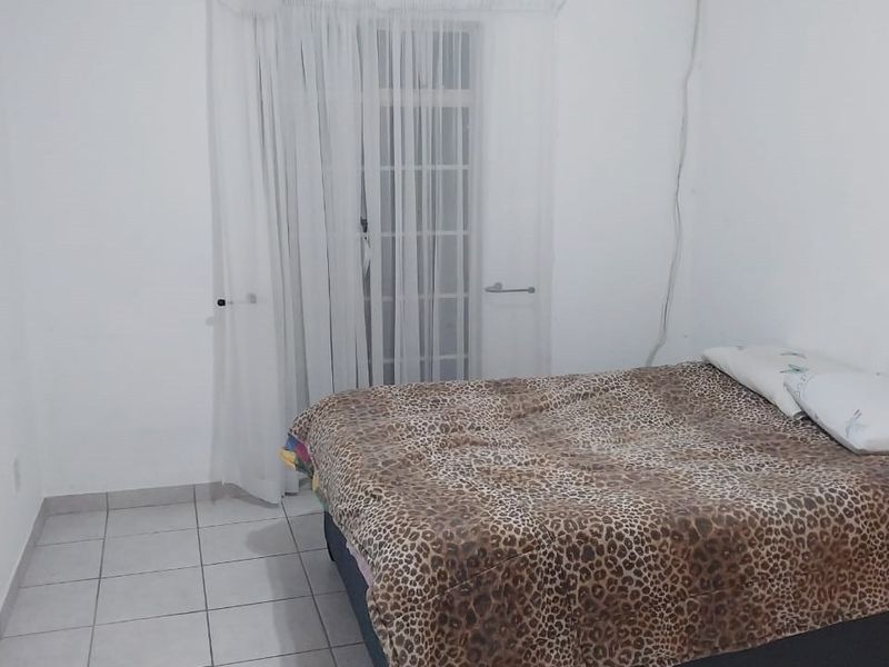 A simple bedroom featuring neutral tiled flooring and a sliding glass door with access to an outdoor area.