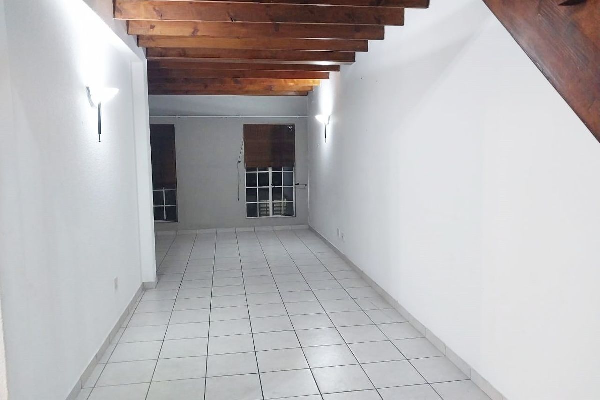 An empty living area featuring exposed timber ceiling beams, tiled flooring, and a wooden staircase, offering a blank canvas for interior design.