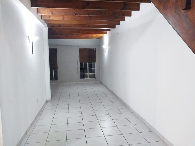 An empty living area featuring exposed timber ceiling beams, tiled flooring, and a wooden staircase, offering a blank canvas for interior design.