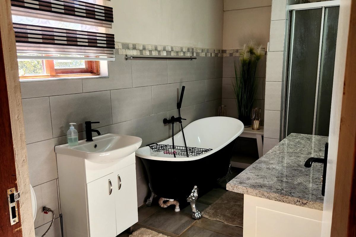 A well-appointed bathroom featuring a modern freestanding bathtub, a separate shower enclosure, a vanity with a granite countertop, and neutral ceramic tiling.