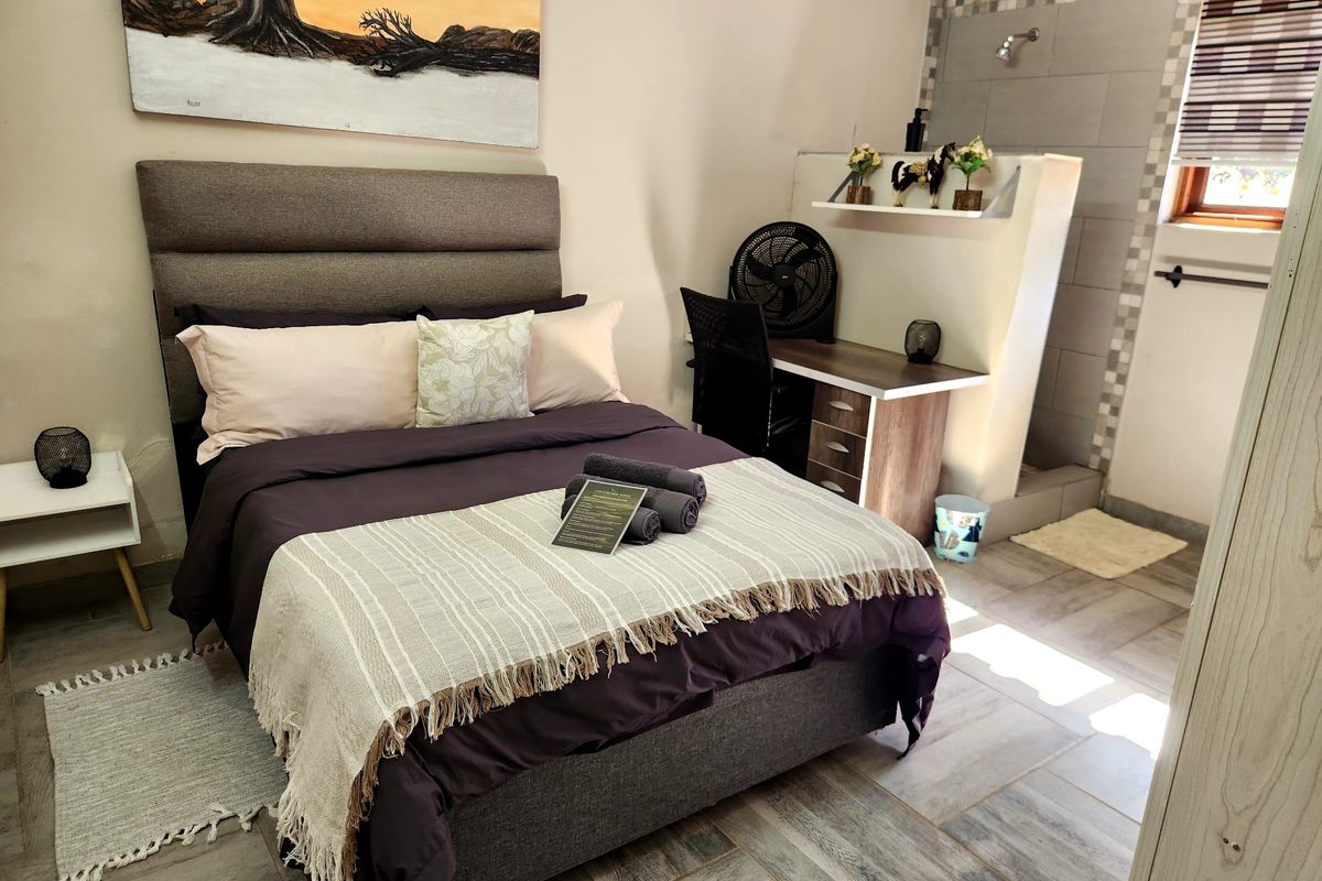 A bedroom featuring an open-plan layout with an integrated shower area, built-in desk, and modern tiled flooring.