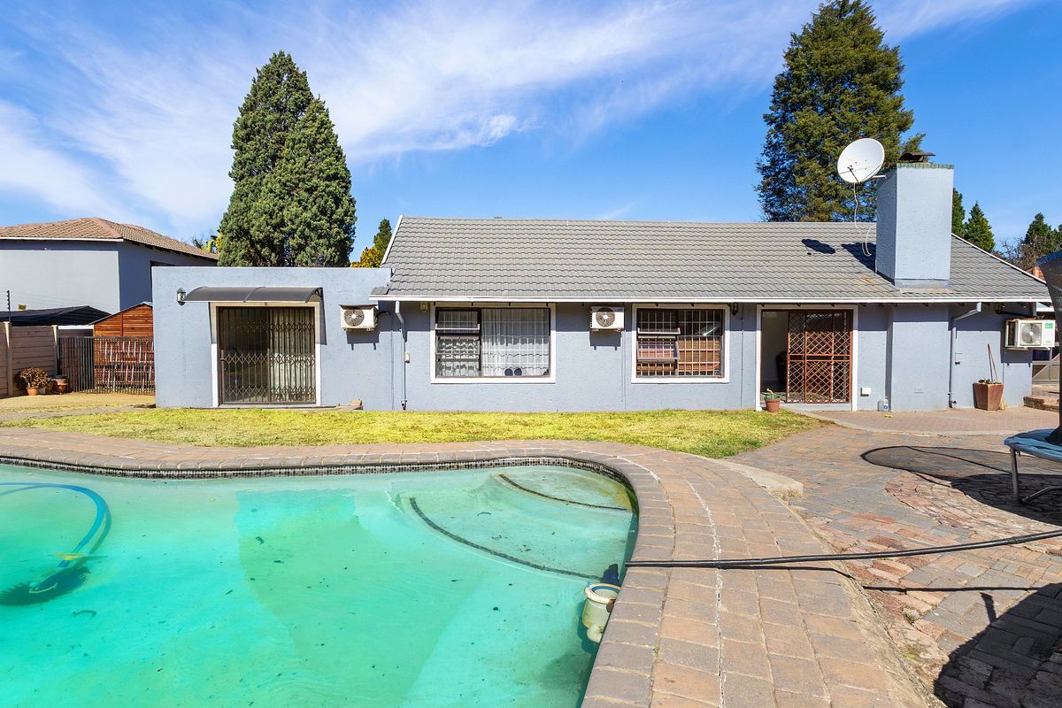 Rear exterior view of the house featuring a swimming pool, paved patio area, and established garden space.