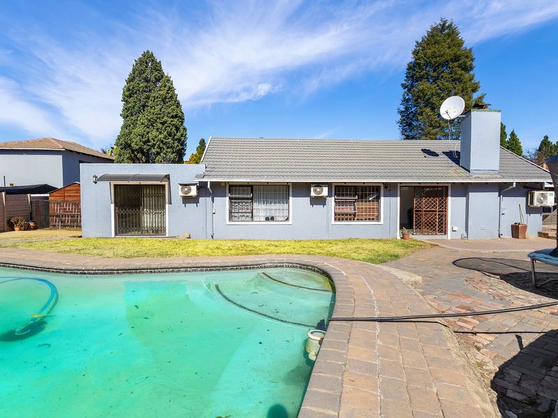 Rear exterior view of the house featuring a swimming pool, paved patio area, and established garden space.