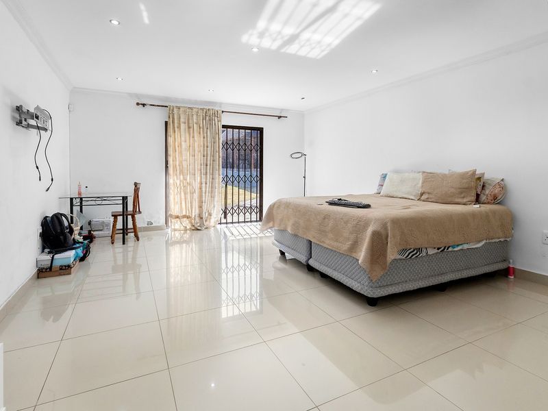 Spacious bedroom featuring polished tile flooring, recessed downlighting, and a sliding glass door with security gate providing direct access to the exterior.