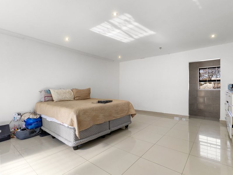 Spacious bedroom featuring neutral tiled flooring, recessed downlighting, and a built-in cupboard, offering a clean and bright living space.