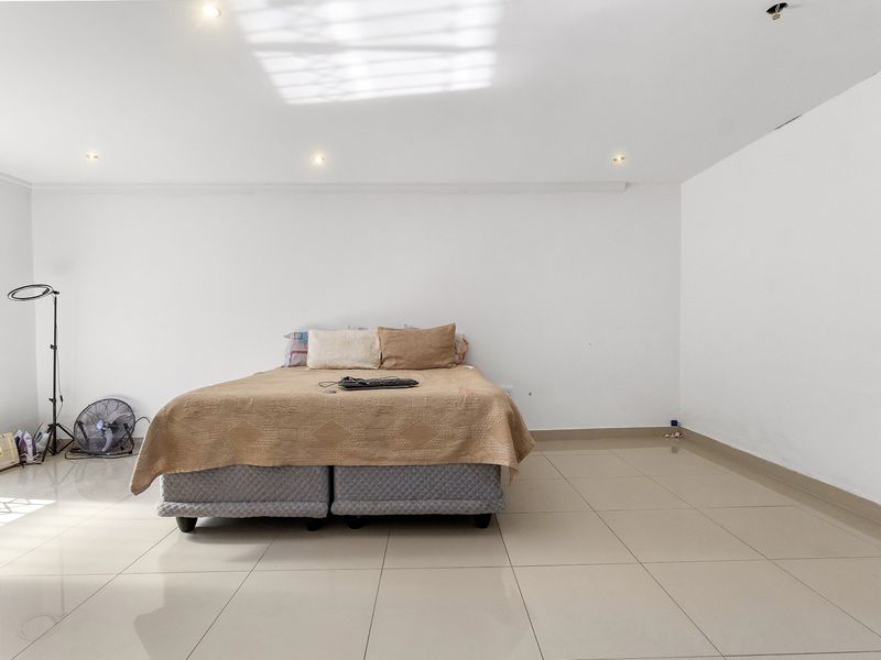 A spacious bedroom featuring neutral tiled flooring and recessed downlighting, offering a clean and simple canvas for personalization.
