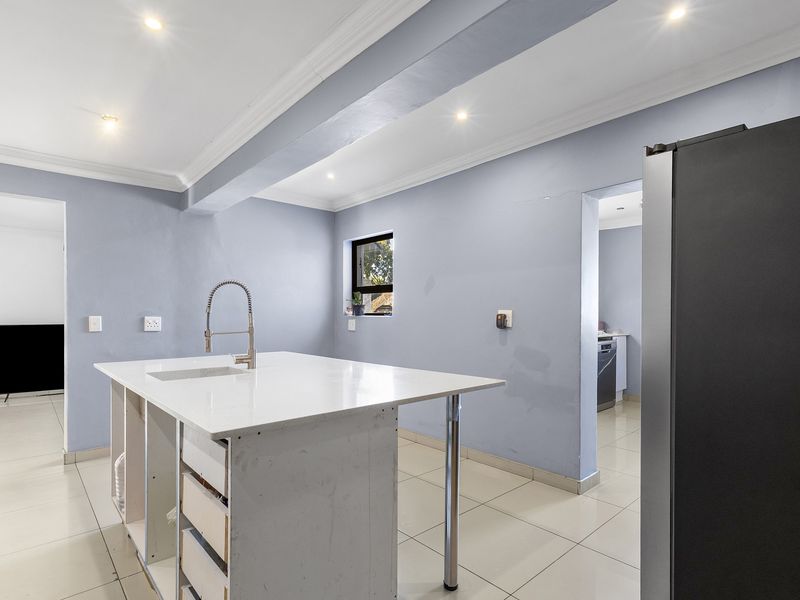 A kitchen area featuring a central island with a sink, tiled flooring, and recessed lighting, currently requiring finishing touches to the cabinetry and wall repairs.