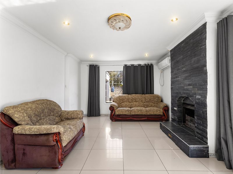 Spacious living room featuring large format floor tiles, a prominent stone-clad fireplace, and a wall-mounted air conditioning unit.