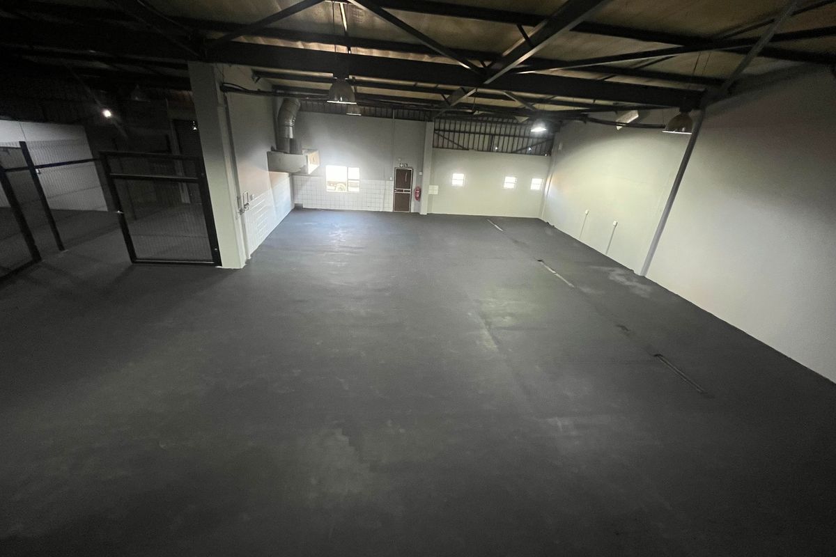 Spacious industrial utility area featuring high exposed steel roof trusses, durable painted concrete flooring, and secure metal gate access.