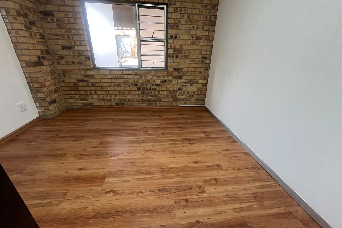 An empty bedroom featuring a characterful exposed brick feature wall, laminate wood flooring, and a sliding window providing natural light.