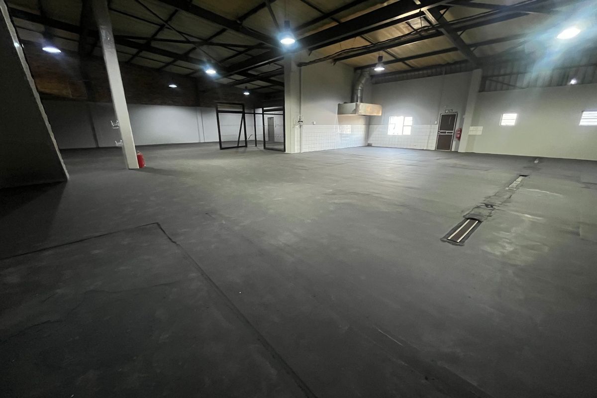 Spacious industrial utility area featuring exposed steel roof trusses, concrete flooring with drainage, and an integrated extractor hood.