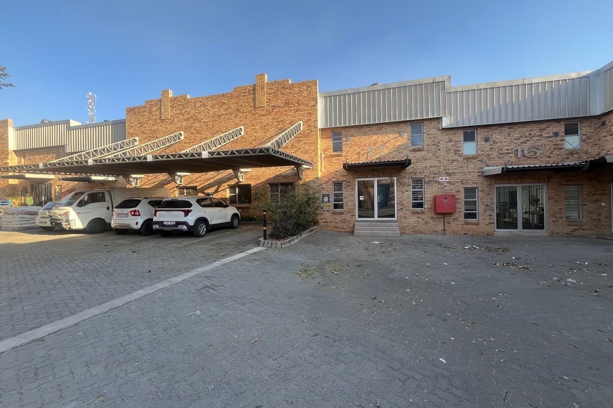 Front elevation of an industrial property featuring a brick facade, metal roofing, covered parking bays, and paved driveway access.