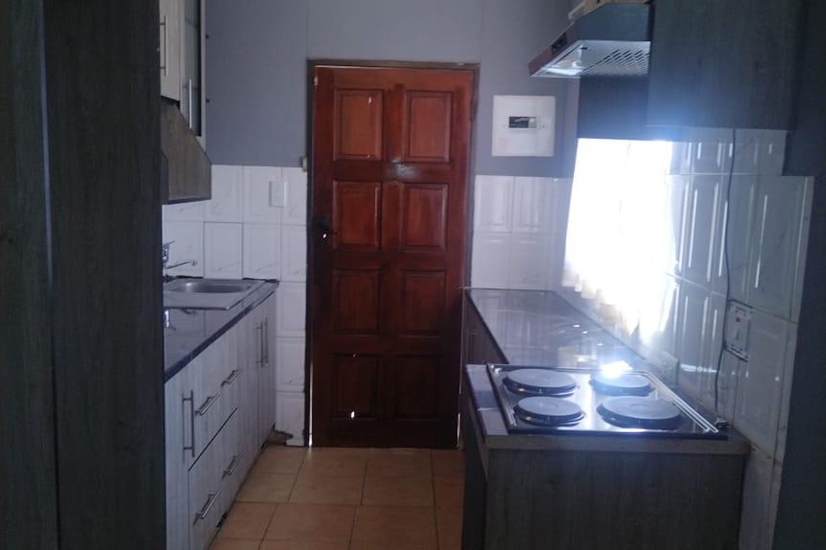 A functional galley-style kitchen featuring built-in cabinetry, an electric hob with extractor fan, tiled splashbacks, and tiled flooring.