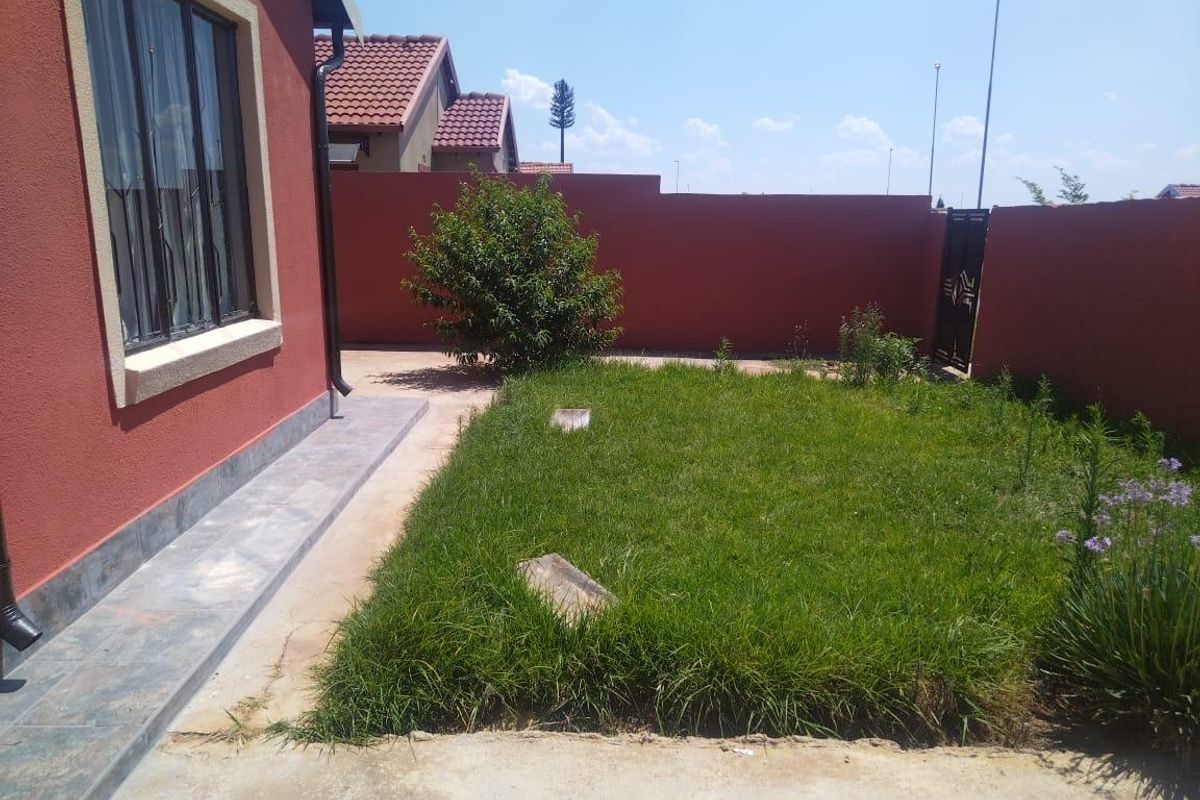 A rear garden area featuring a tiled patio, perimeter boundary wall, and a small lawn space.