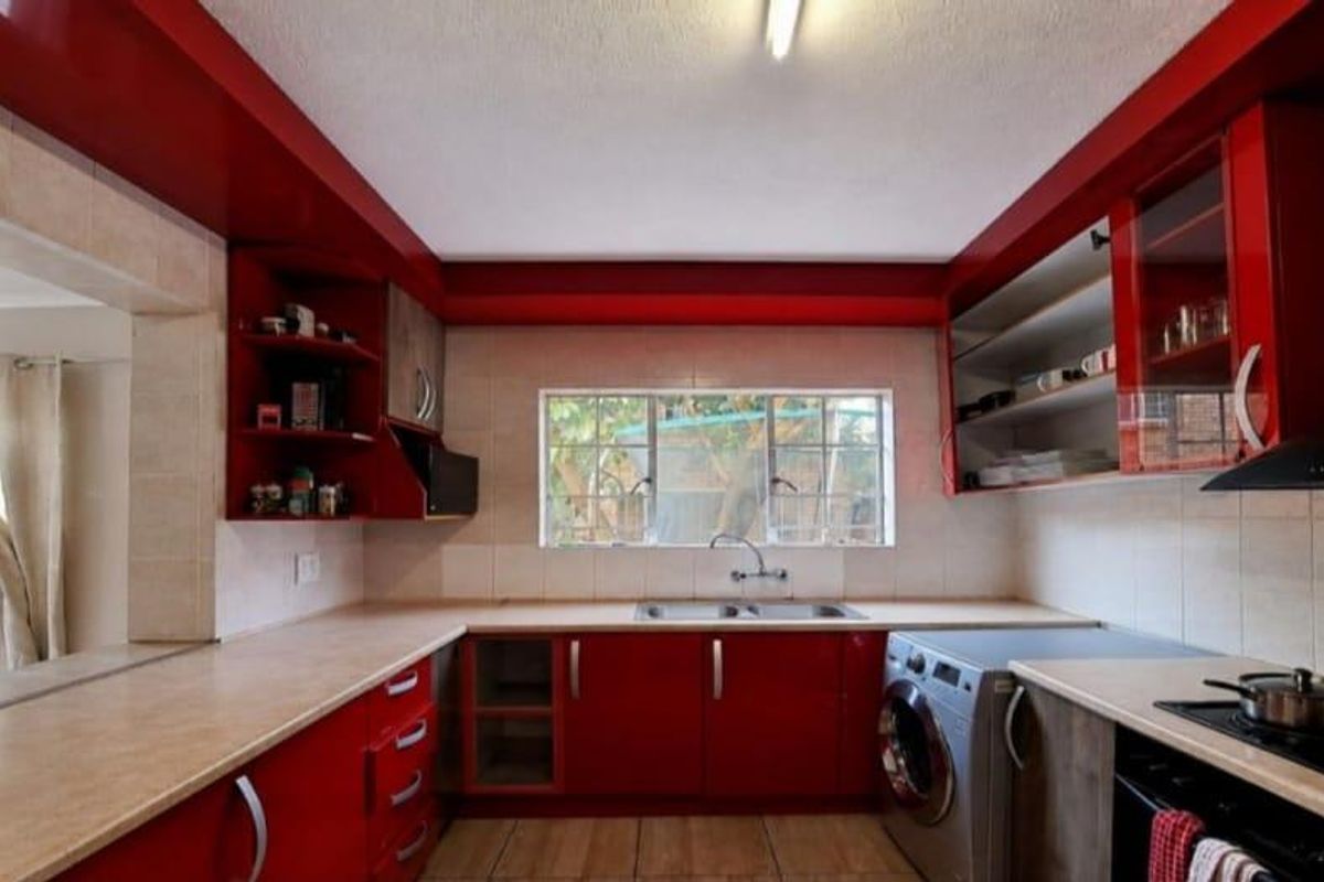 A functional kitchen featuring red cabinetry, laminate countertops, a double basin sink, and integrated cooking appliances with direct access to the outdoor area.