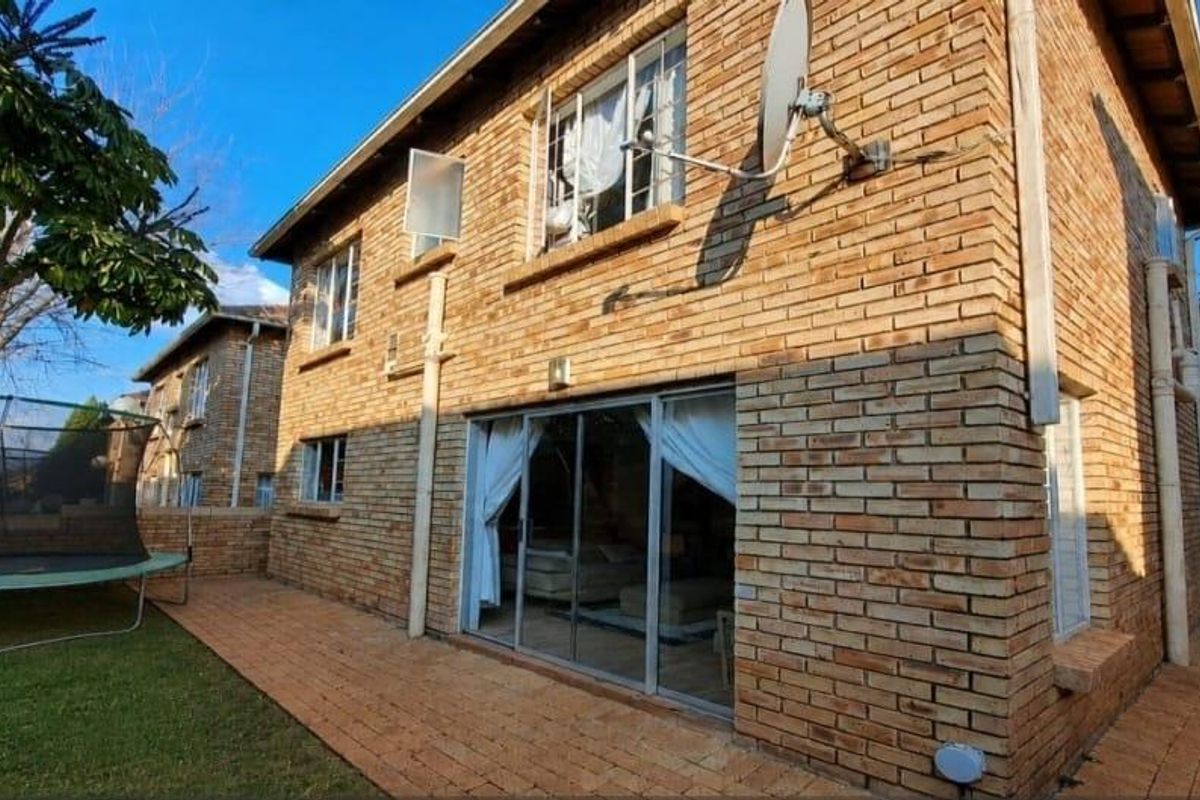 Rear view of the townhouse featuring a face brick facade, paved patio area, and sliding glass doors leading into the living space.