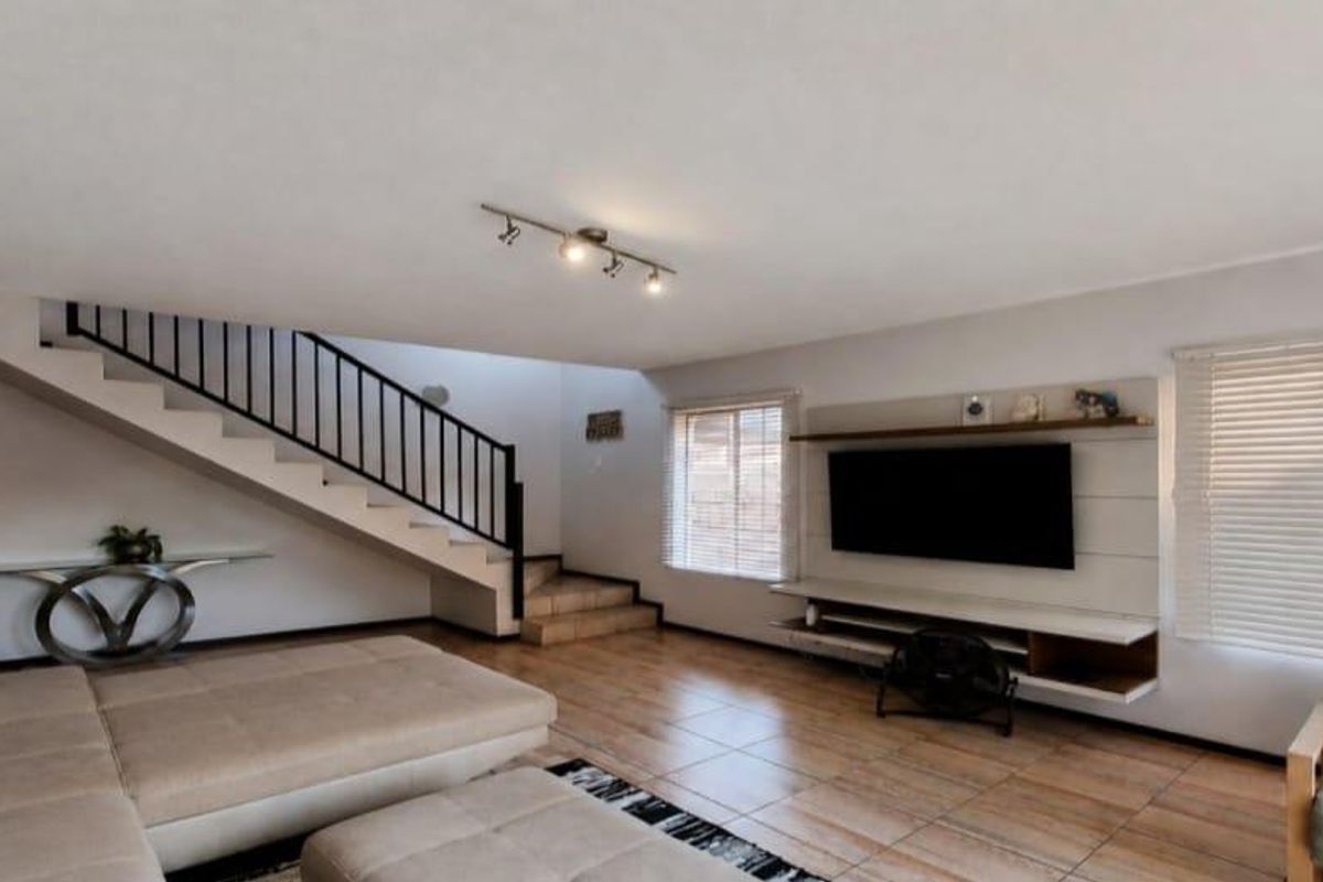 Spacious living room featuring tiled flooring, a built-in media unit, and a staircase with a metal balustrade.