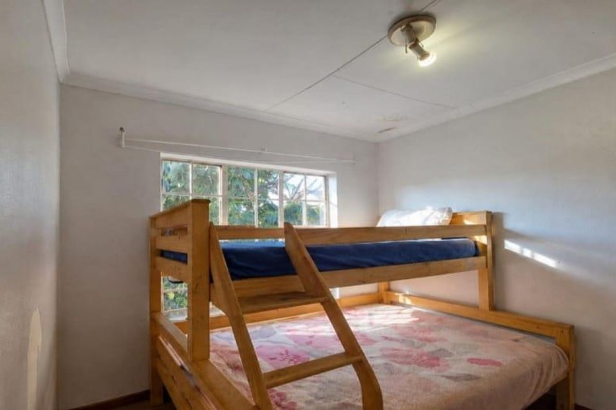 A compact bedroom featuring a window, ceiling light fixture, and coving, showing signs of wear on the walls and ceiling.