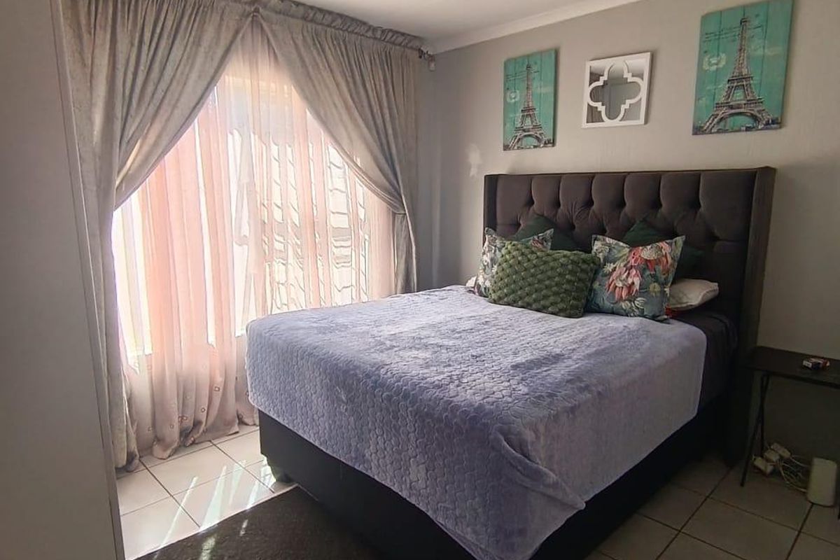 A bedroom featuring tiled flooring, neutral wall finishes, and a large window with curtain tracks, providing natural light to the space.