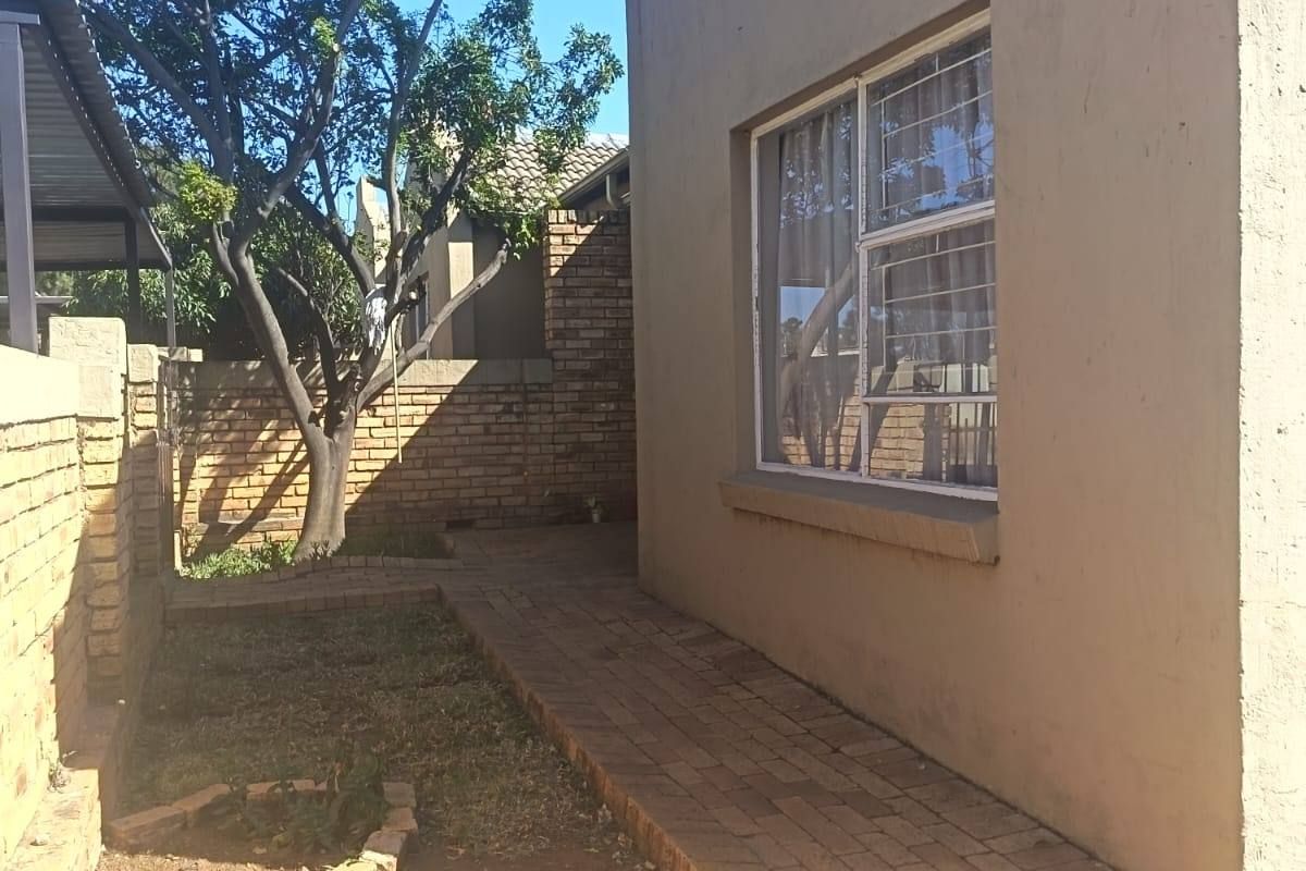 Rear exterior view of the townhouse featuring a paved walkway, brick boundary wall, and established garden area with security-fitted windows.