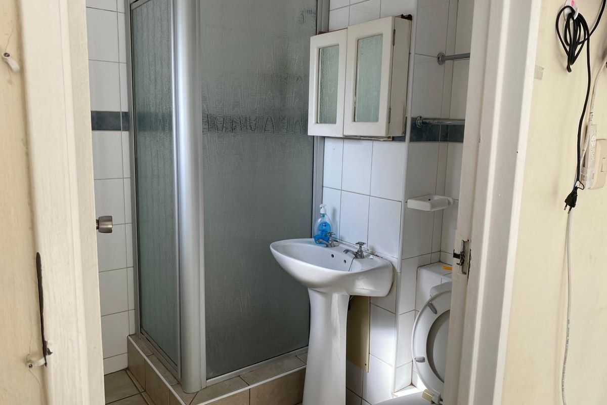 A compact bathroom featuring a shower enclosure, pedestal basin, and toilet, with dated wall tiling and cabinetry in need of modernization.