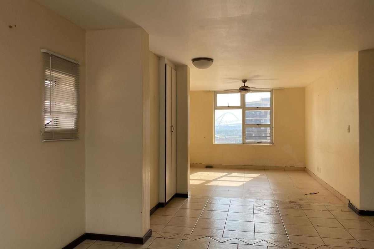 An empty, open-plan living area featuring tiled flooring, a ceiling fan, and built-in storage, offering a blank canvas for renovation.