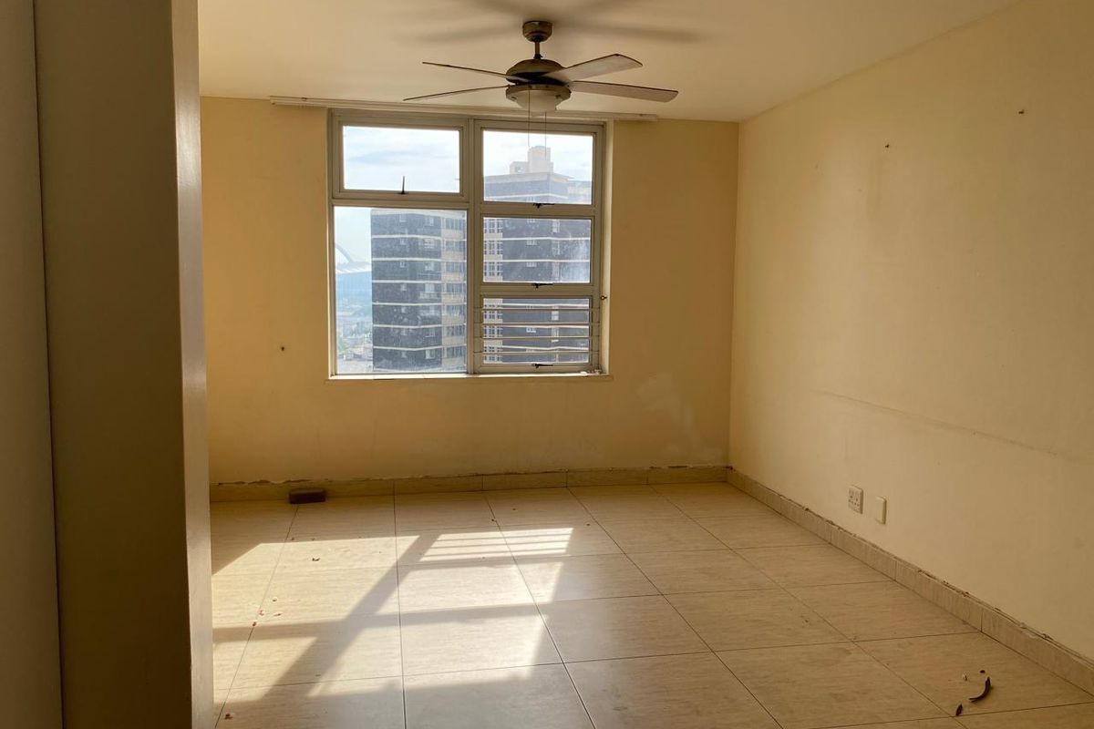 An empty bedroom featuring tiled flooring, a ceiling fan, and large windows with urban views. The space requires minor cosmetic updates to walls and skirting.