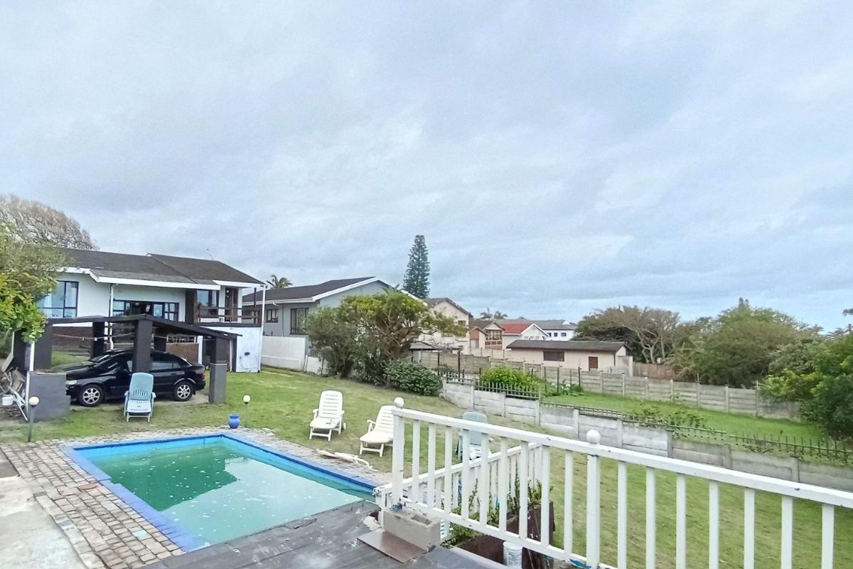 Rear exterior view featuring a swimming pool, lawn area, and perimeter boundary wall, viewed from an elevated deck with a white balustrade.