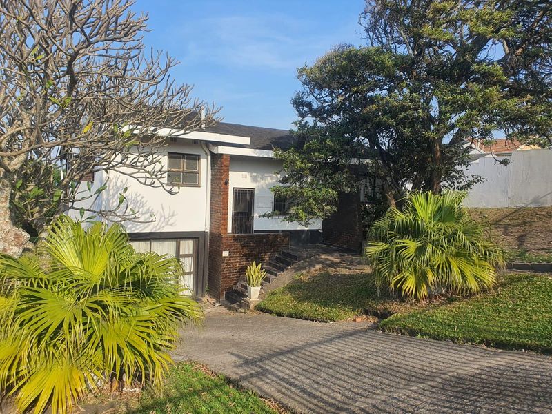 Front elevation of a multi-level house featuring a brick and plaster facade, concrete driveway, and established garden surroundings.