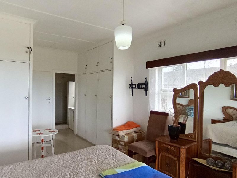 A bedroom featuring extensive built-in cupboard storage, a pendant light fixture, and a wall-mounted TV bracket, with an adjoining en-suite bathroom visible.