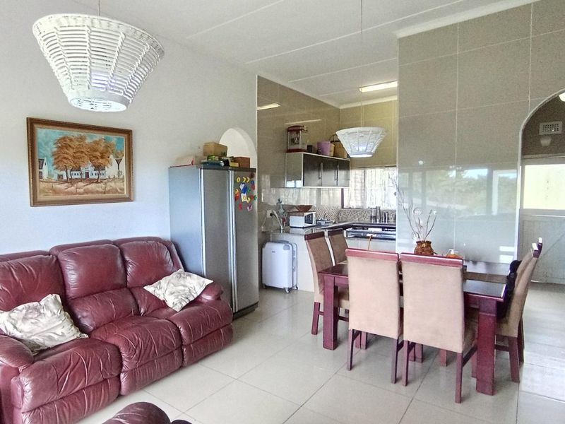 Open-plan living and dining area featuring tiled flooring and a functional kitchen with built-in cabinetry and integrated appliances.