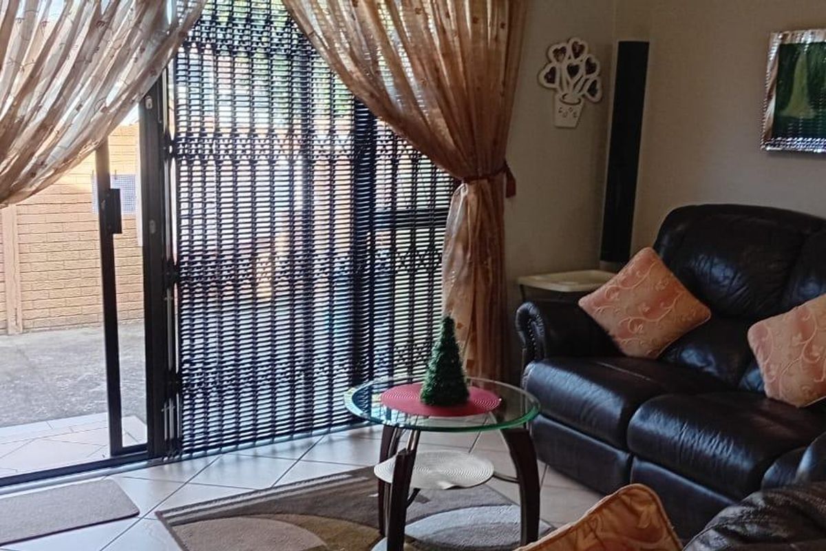 A living room featuring tiled flooring and a sliding glass door with a security gate, providing direct access to the outdoor area.