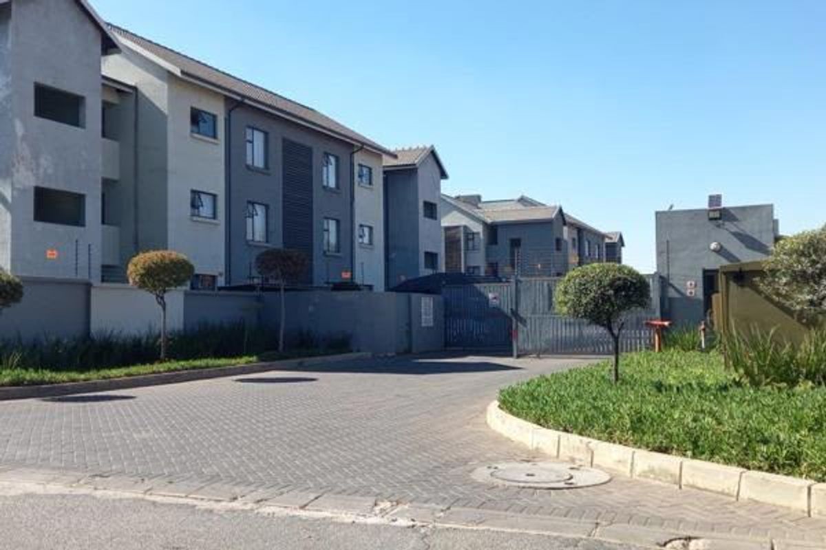 Front view of an apartment complex featuring a paved driveway, secure gated entrance, and well-maintained perimeter walls with electric fencing.