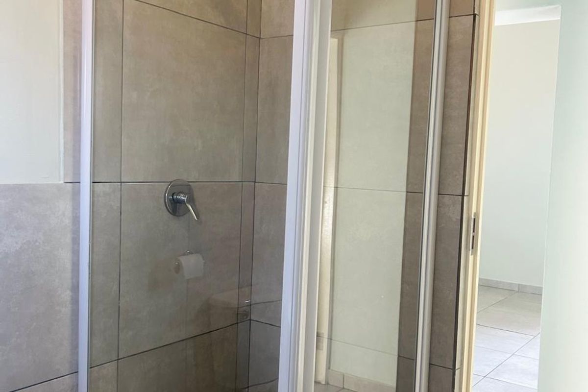 A clean, modern bathroom featuring a glass-enclosed shower with neutral wall and floor tiling.
