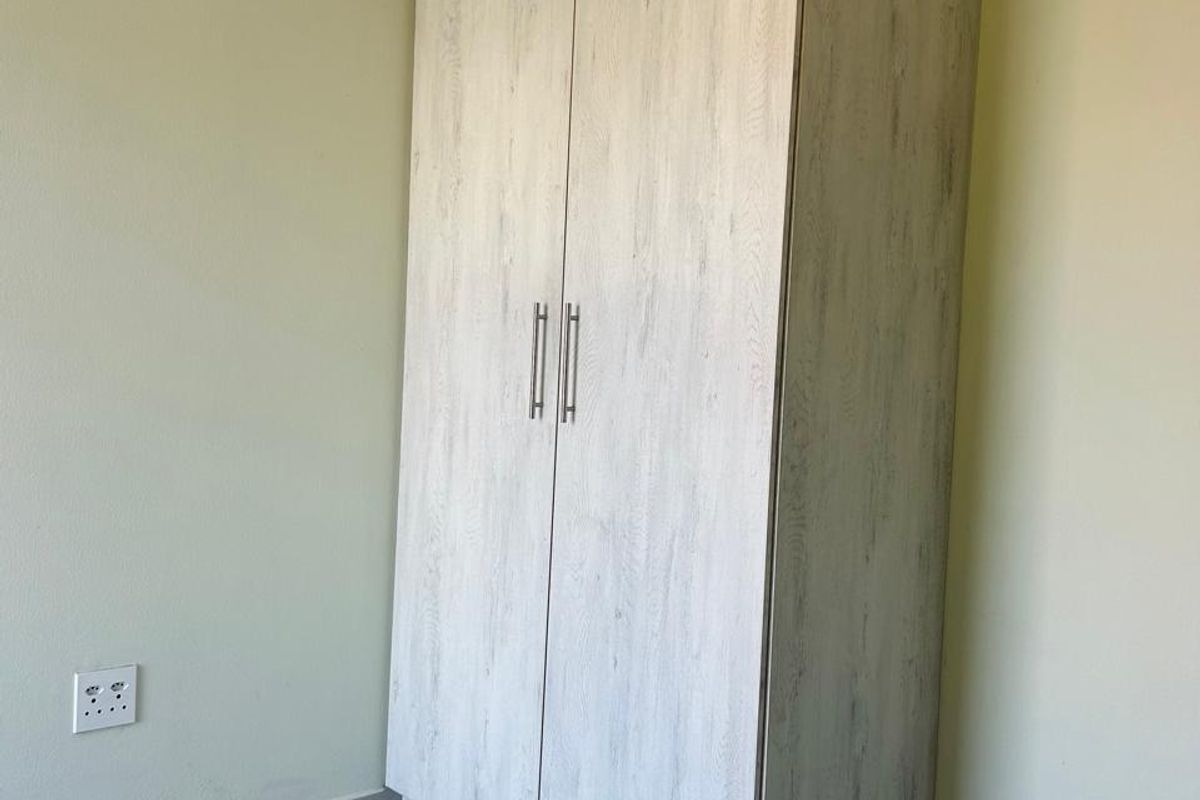 A bedroom corner featuring a light wood-grain built-in wardrobe, neutral wall paint, and tiled flooring.