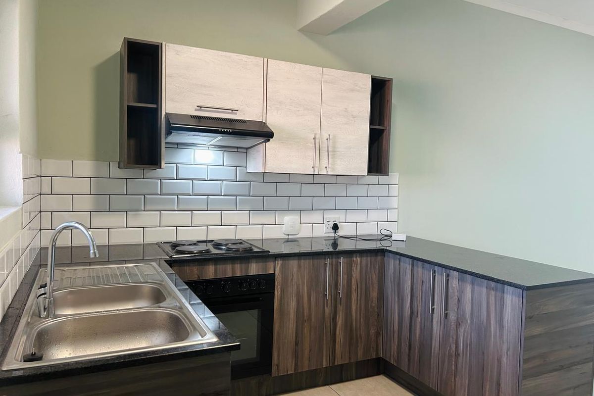 A modern, well-maintained kitchen featuring dark wood-grain lower cabinets, light wood-effect upper cabinets, black countertops, and a classic white subway tile backsplash.