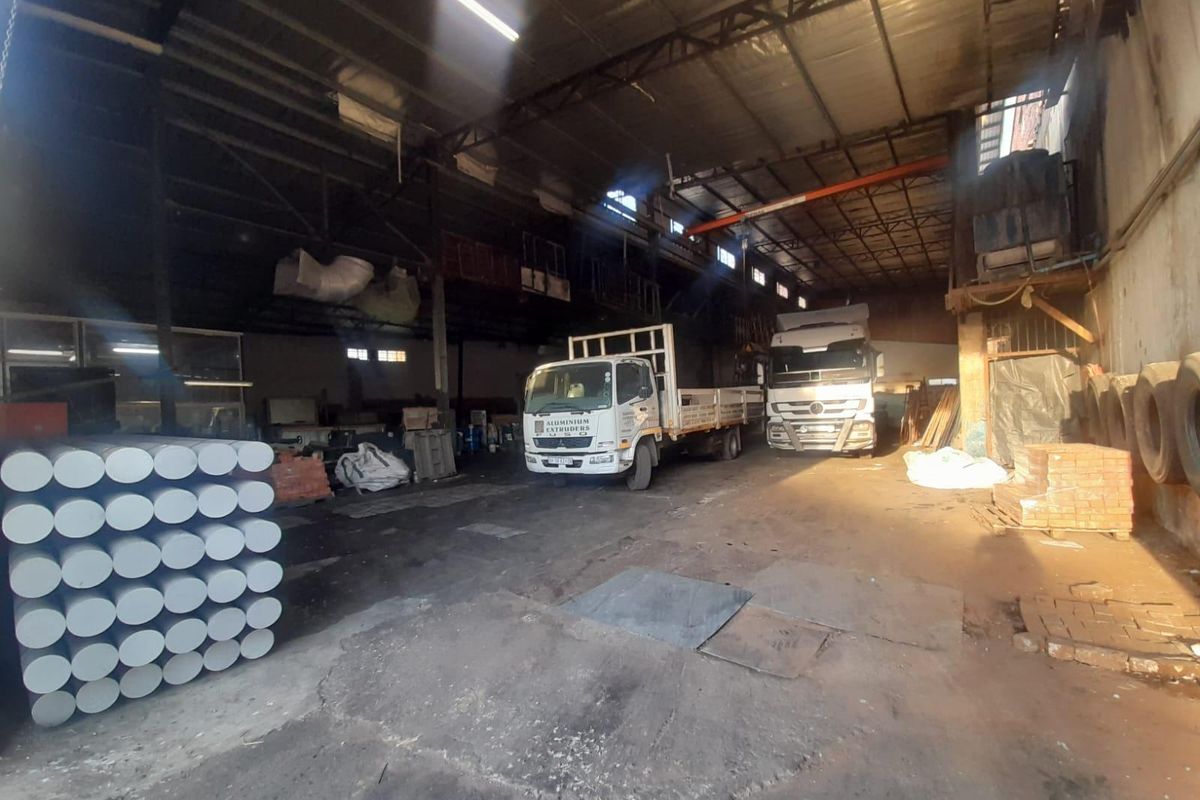 Spacious industrial warehouse facility featuring high ceilings, exposed steel roof trusses, concrete flooring, and a mezzanine level suitable for storage or manufacturing operations.