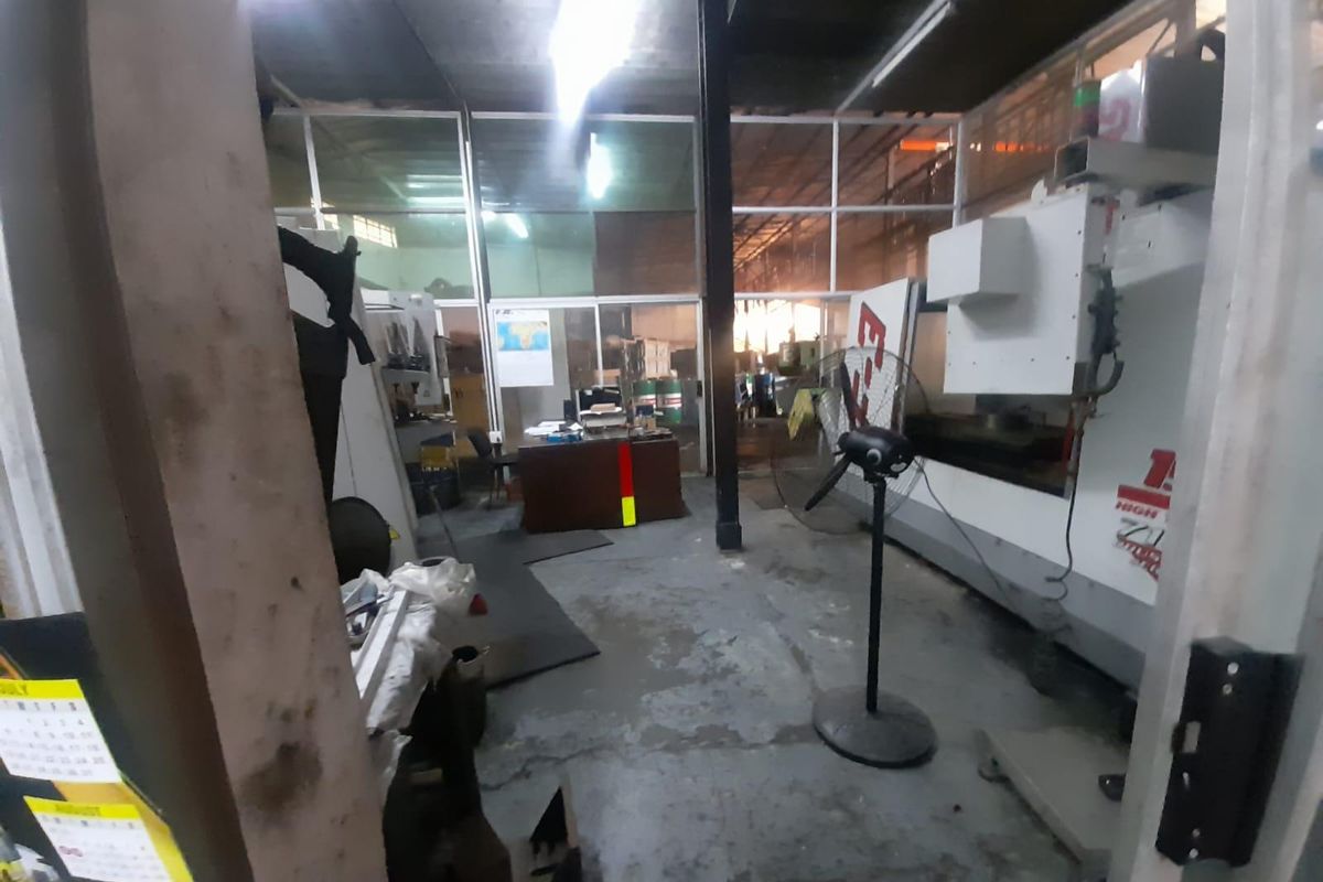 Industrial workspace featuring concrete flooring, glass partitioning, and heavy machinery, suitable for manufacturing or workshop operations.