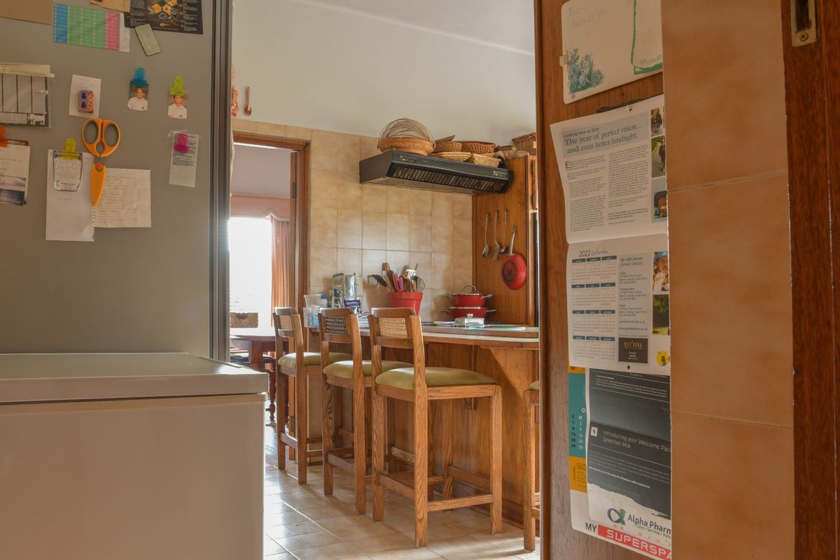 A functional kitchen featuring a breakfast bar, wooden cabinetry, and tiled splashback, viewed through a doorway.