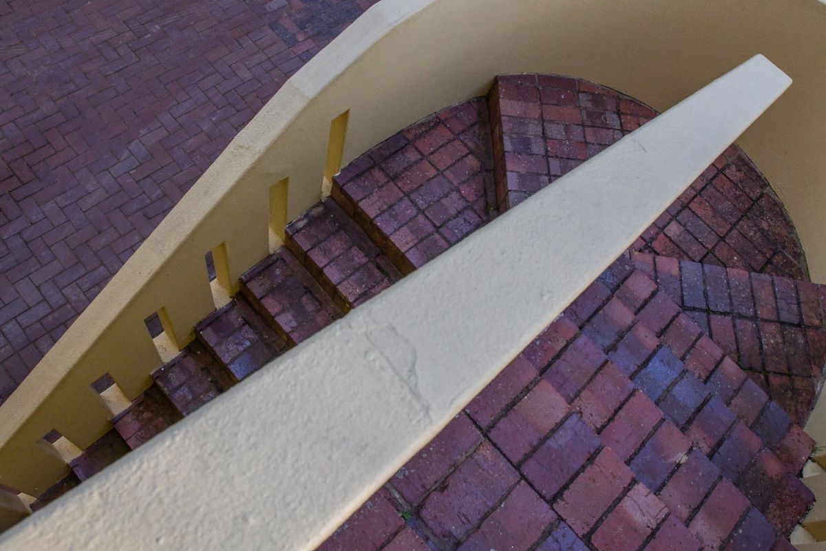 An elevated view of a curved outdoor brick staircase featuring a solid concrete balustrade and matching brick paved landing.