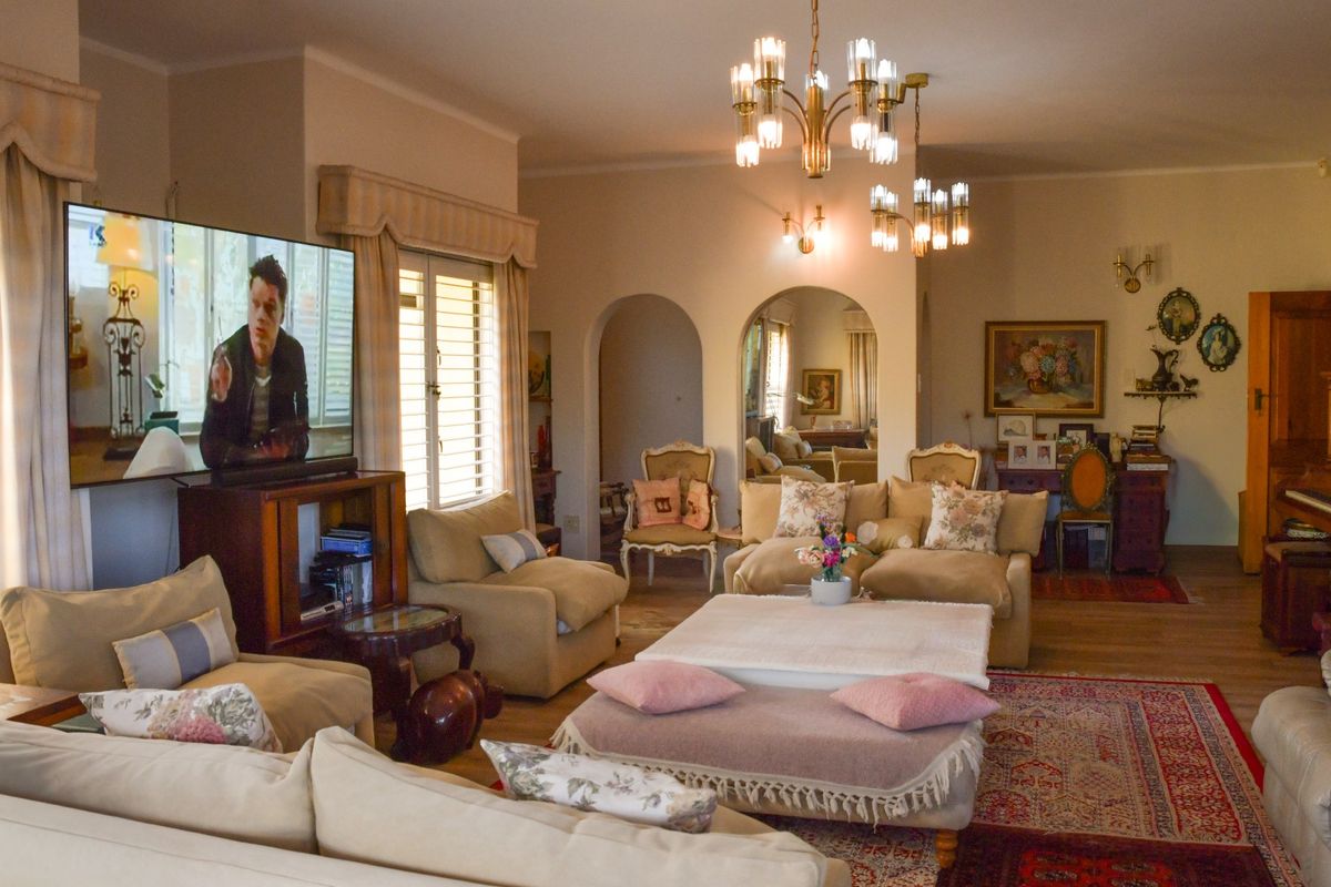 A spacious living room featuring classic arched doorways, elegant chandeliers, wall sconces, and timber window shutters, offering a traditional and comfortable atmosphere.