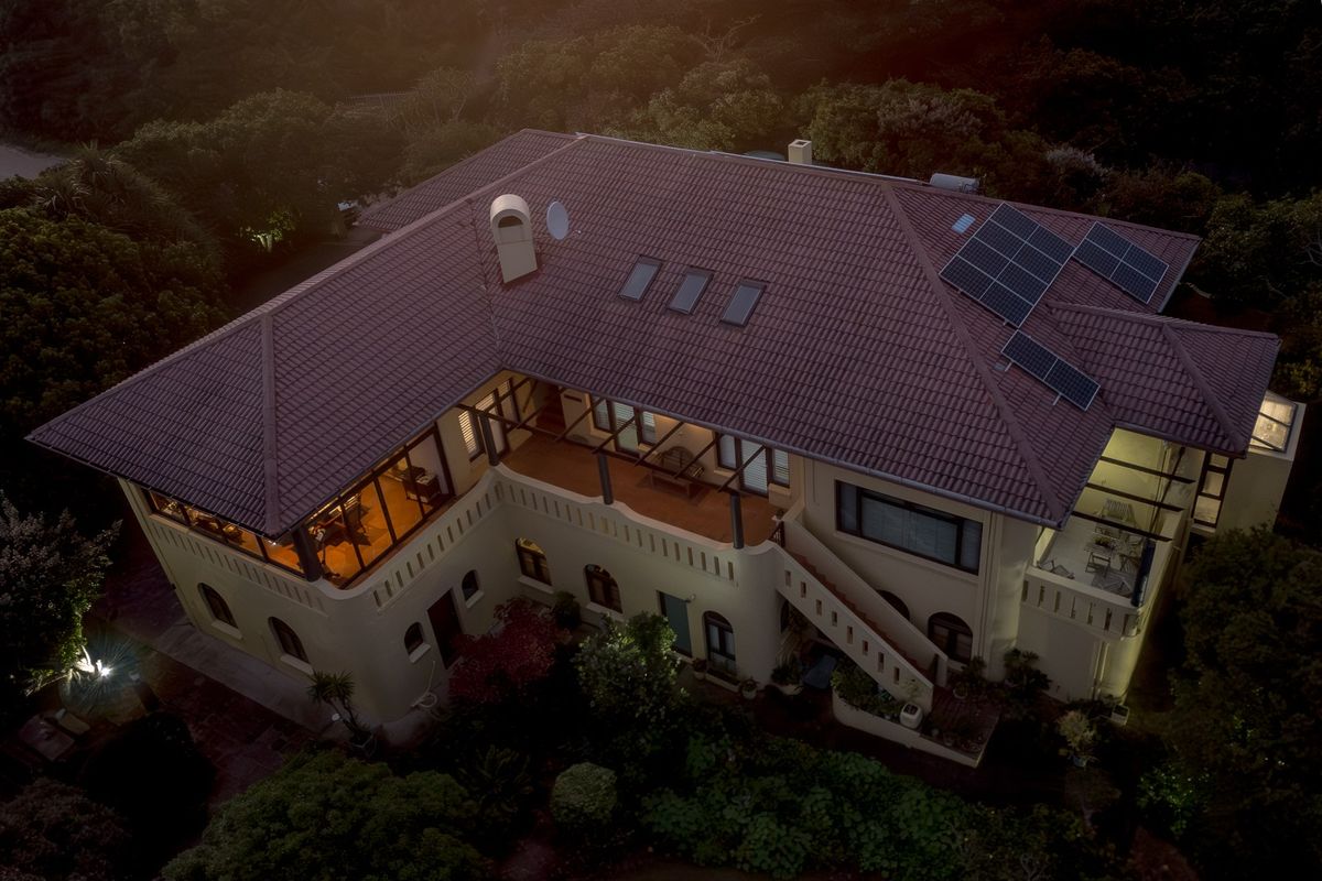 Aerial view of a multi-level residence featuring a tiled roof, integrated solar panels, skylights, and an expansive balcony with an external staircase.