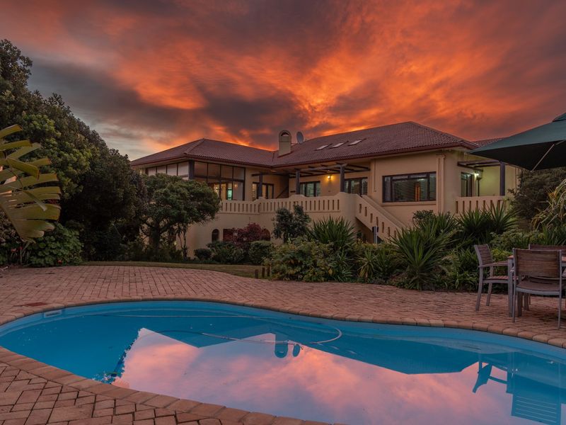 A beautiful rear exterior view of the house featuring a swimming pool, paved deck, and a spacious balcony at sunset.