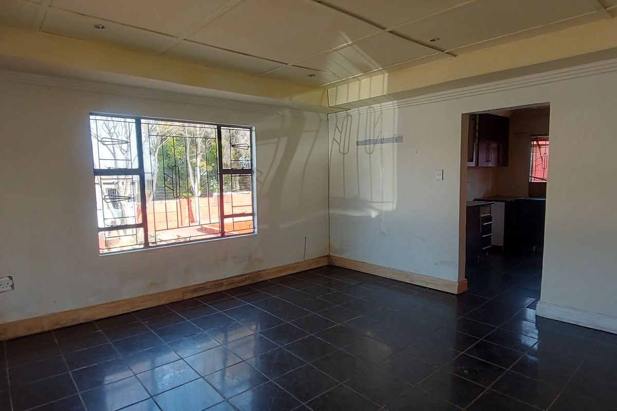 An empty living room featuring dark tiled flooring, recessed ceiling detail, and security bars on the windows, with an open transition to the kitchen area.