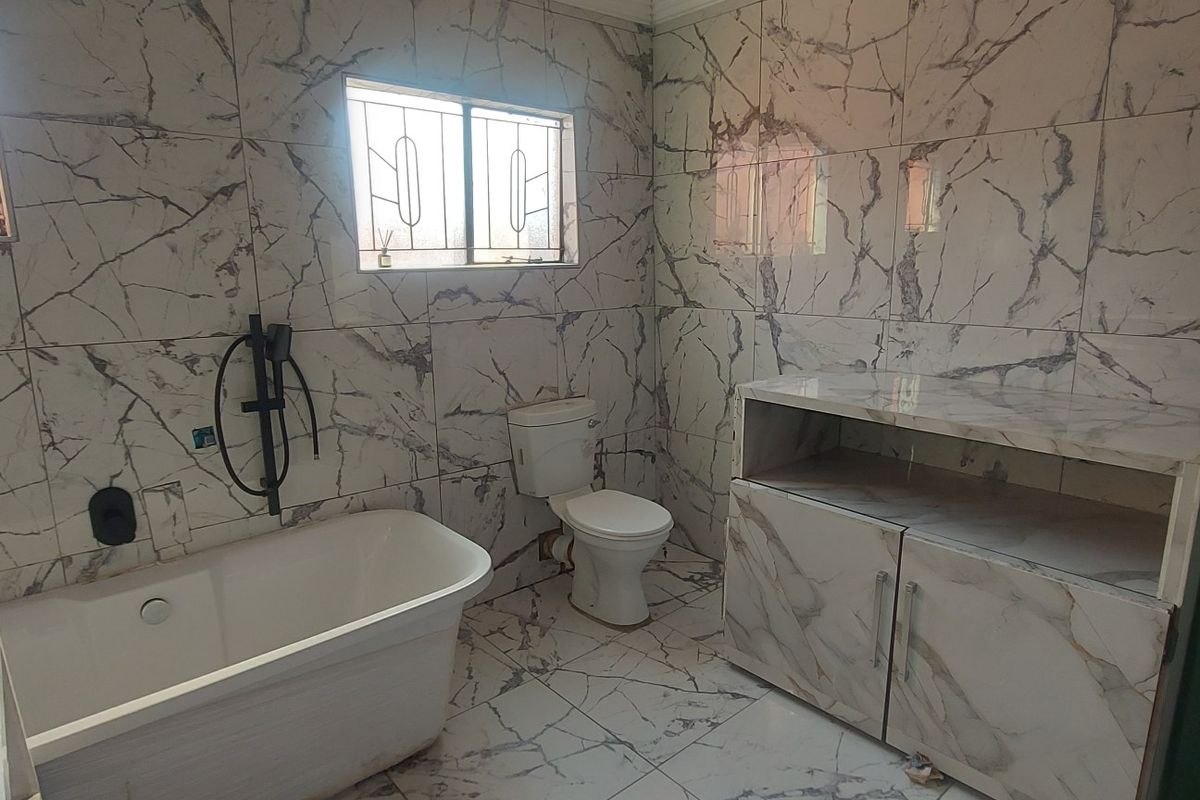 A modern bathroom featuring marble-effect wall and floor tiles, a freestanding bathtub, a toilet, and a built-in vanity cabinet.